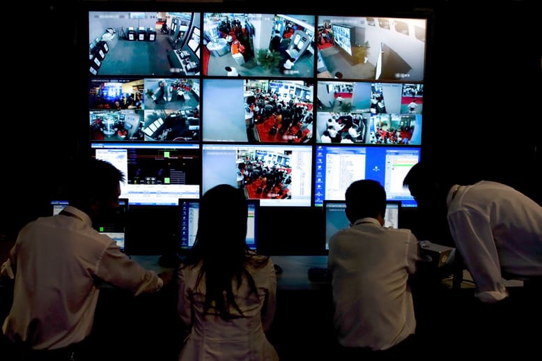 A group of people watching multiple monitors in a room.