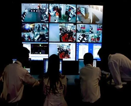 A group of people watching multiple monitors in a room.